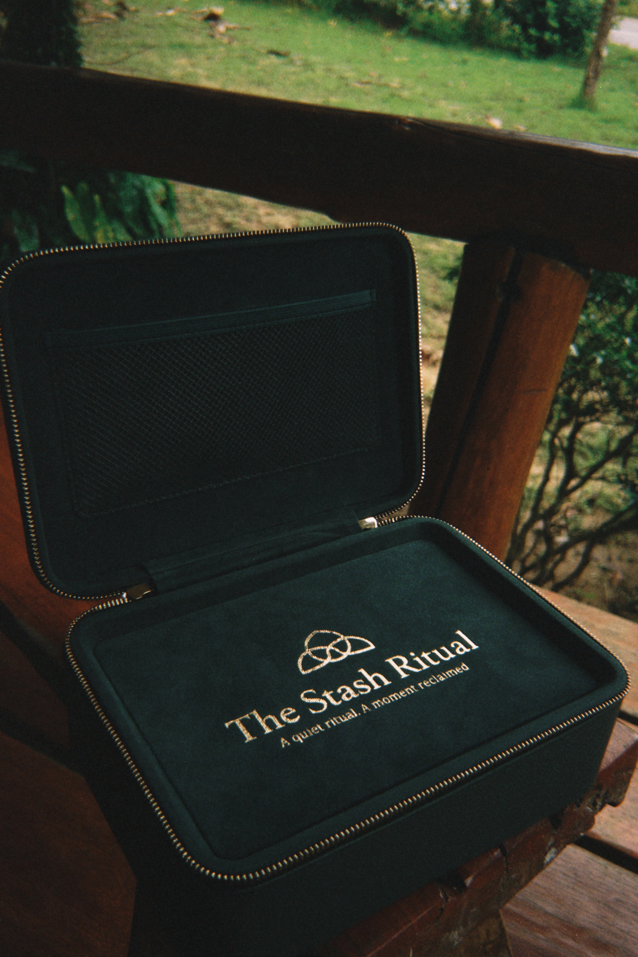 The Stash Ritual case open, showing structured interior compartments and the branded logo tray beside a thermos on a patterned rug